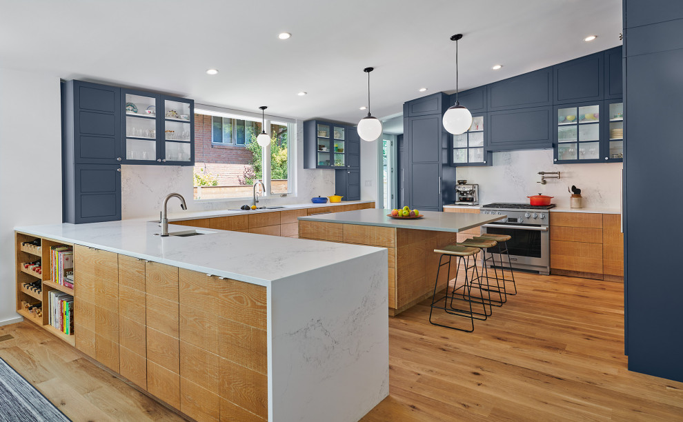 Large midcentury u-shaped kitchen in DC Metro with an undermount sink, flat-panel cabinets, light wood cabinets, quartz benchtops, white splashback, engineered quartz splashback, light hardwood floors, with island and vaulted.