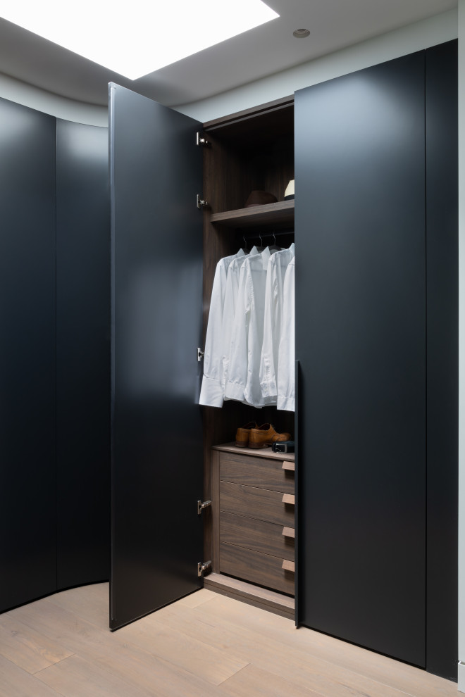 Foto de vestidor unisex minimalista grande con armarios con paneles lisos, puertas de armario negras y suelo de madera clara