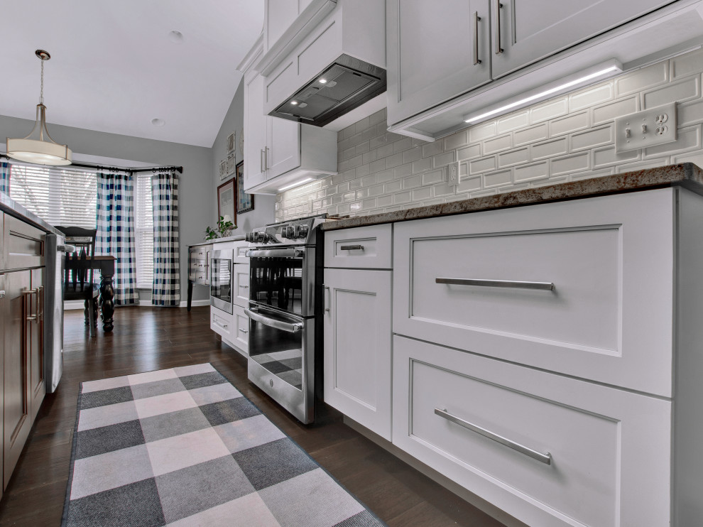 Eat-in kitchen - mid-sized transitional medium tone wood floor, brown floor and vaulted ceiling eat-in kitchen idea in St Louis with an undermount sink, shaker cabinets, white cabinets, granite countertops, white backsplash, subway tile backsplash, stainless steel appliances, an island and multicolored countertops