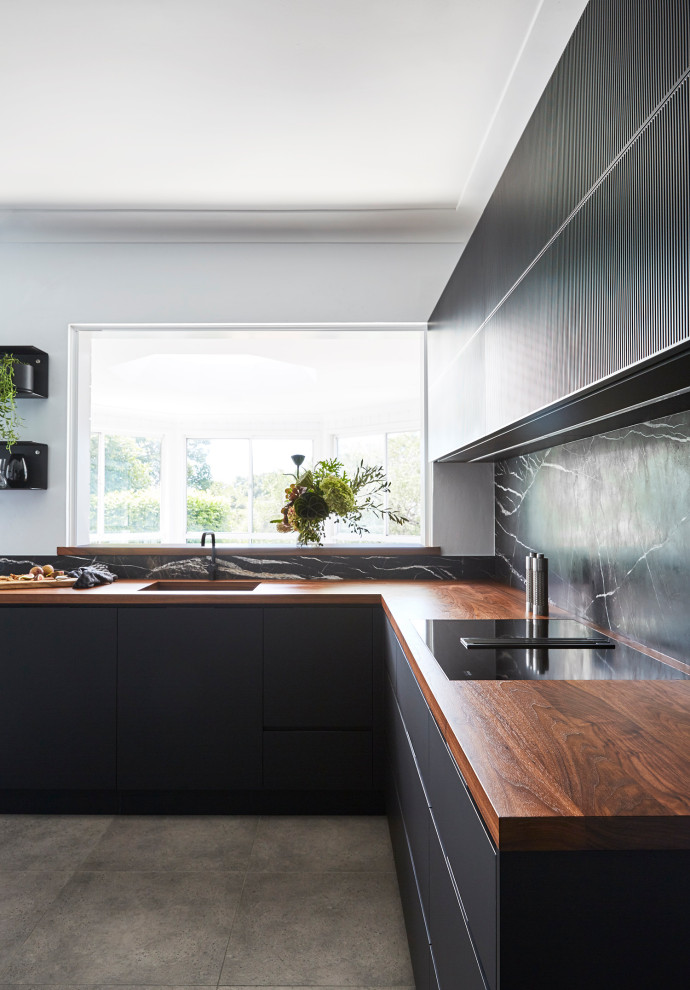 Inspiration for a medium sized contemporary l-shaped enclosed kitchen in Sydney with a single-bowl sink, flat-panel cabinets, black cabinets, wood worktops, black splashback, marble splashback, black appliances, porcelain flooring, no island, grey floors and brown worktops.
