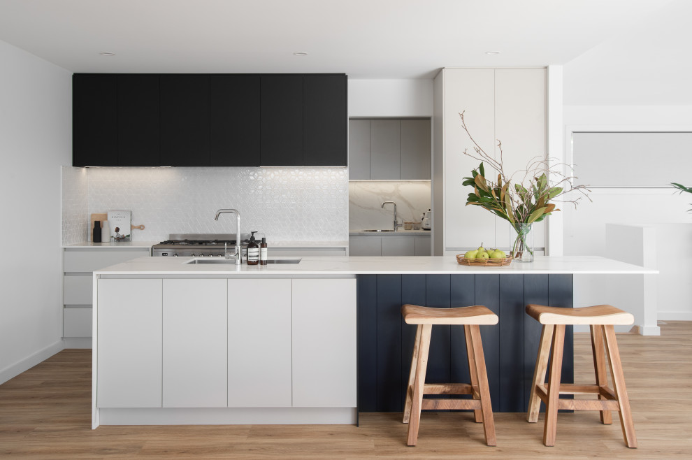 This is an example of a contemporary kitchen in Hobart with an undermount sink, flat-panel cabinets, white cabinets, white splashback, stainless steel appliances, light hardwood floors, with island and white benchtop.