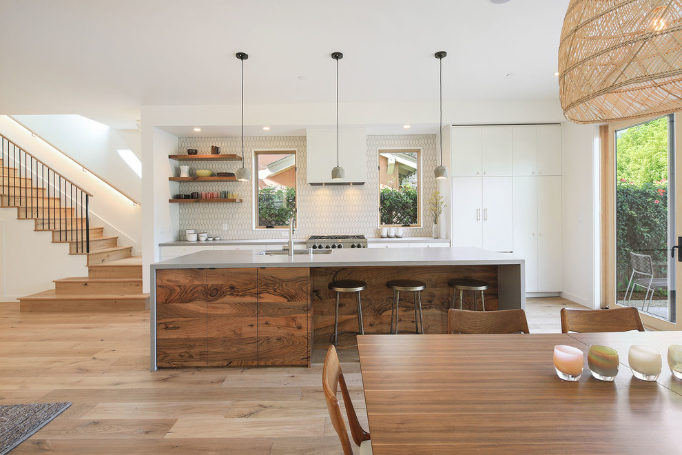 Contemporary galley kitchen in San Francisco with an undermount sink, flat-panel cabinets, white cabinets, white splashback, stainless steel appliances, light hardwood floors, with island, beige floor and grey benchtop.