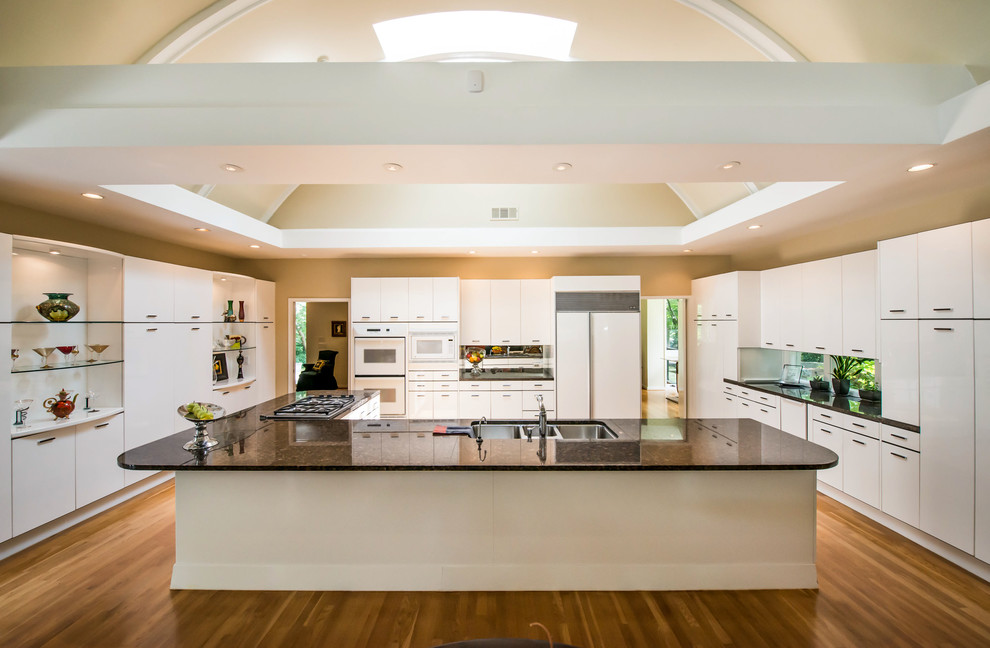 Contemporary u-shaped kitchen in Atlanta with a triple-bowl sink, flat-panel cabinets, white cabinets, granite benchtops and white appliances.