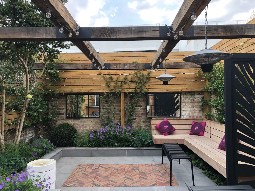 Photo of a small industrial back patio in London with brick paving and a pergola.