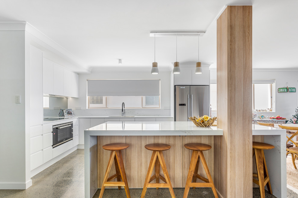 Mid-sized beach style l-shaped eat-in kitchen in Gold Coast - Tweed with flat-panel cabinets, white cabinets, quartz benchtops, grey splashback, mirror splashback, stainless steel appliances, with island and white benchtop.