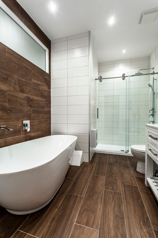 Inspiration for a mid-sized master bathroom in Montreal with an integrated sink, shaker cabinets, white cabinets, solid surface benchtops, a freestanding tub, an alcove shower, a two-piece toilet, white tile, porcelain tile, brown walls and porcelain floors.