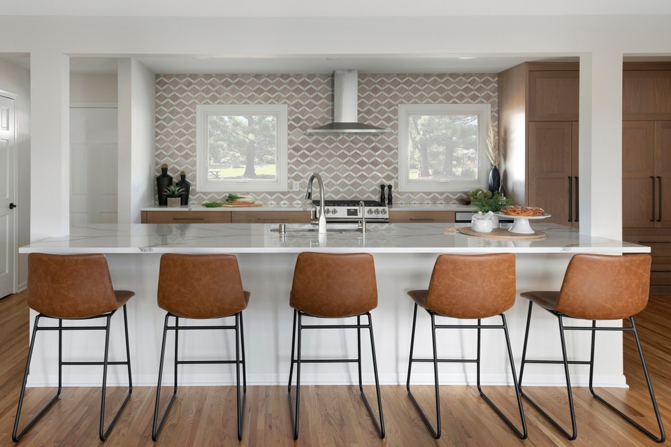 This is an example of a large midcentury single-wall eat-in kitchen in Minneapolis with an undermount sink, shaker cabinets, brown cabinets, quartzite benchtops, beige splashback, marble splashback, stainless steel appliances, medium hardwood floors, with island, brown floor and white benchtop.