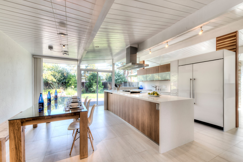 Inspiration for a mid-sized transitional single-wall porcelain tile eat-in kitchen remodel in Nice with a single-bowl sink, flat-panel cabinets, white cabinets, solid surface countertops, white backsplash, porcelain backsplash, paneled appliances and an island