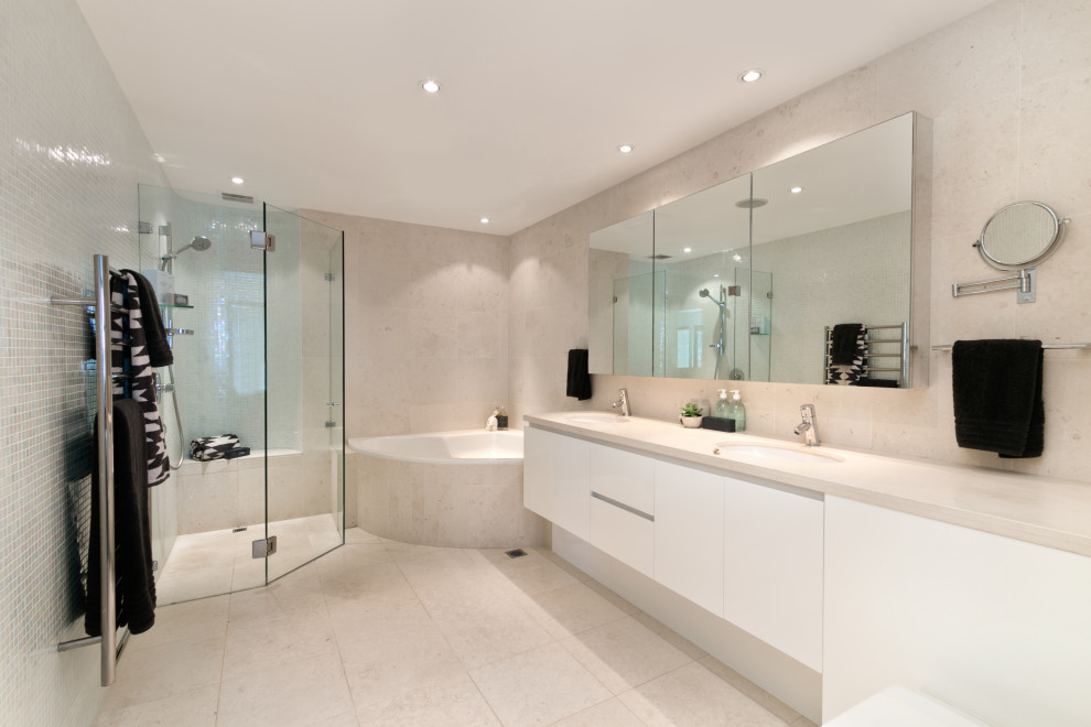 Photo of a large contemporary master bathroom in Houston with flat-panel cabinets, white cabinets, a corner tub, a corner shower, beige tile, an undermount sink, beige floor, a hinged shower door and beige benchtops.