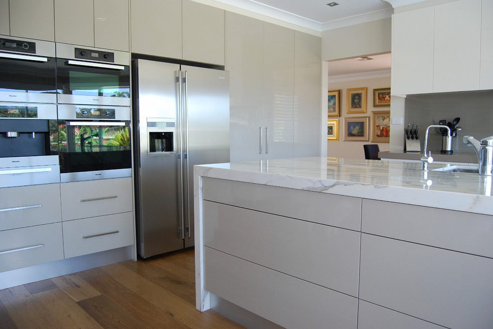 Large contemporary l-shaped kitchen pantry in Sydney with an undermount sink, flat-panel cabinets, green cabinets, marble benchtops, green splashback, glass sheet splashback, stainless steel appliances, medium hardwood floors and with island.