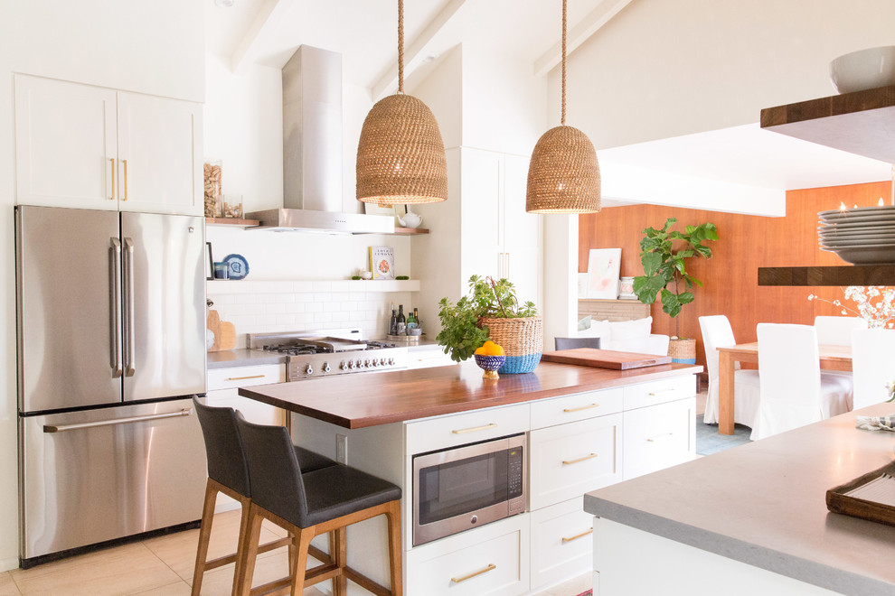 Photo of a beach style galley kitchen in Other with shaker cabinets, white cabinets, white splashback, subway tile splashback, stainless steel appliances, with island and beige floor.