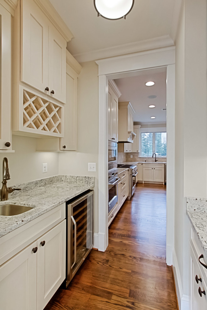 Inspiration for a small arts and crafts galley wet bar in DC Metro with an undermount sink, recessed-panel cabinets, white cabinets, granite benchtops, white splashback and dark hardwood floors.