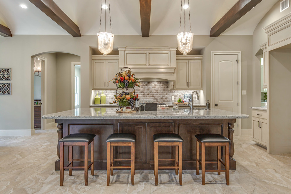 This is an example of a large mediterranean l-shaped eat-in kitchen in Houston with beige cabinets, beige splashback, with island, beige floor, granite benchtops, an undermount sink, recessed-panel cabinets, ceramic splashback, stainless steel appliances and ceramic floors.