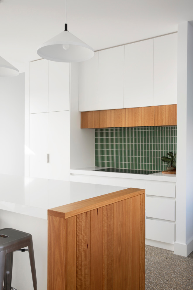 Mid-sized beach style l-shaped open plan kitchen in Melbourne with an undermount sink, flat-panel cabinets, white cabinets, quartz benchtops, green splashback, ceramic splashback, panelled appliances, concrete floors, with island, grey floor and white benchtop.