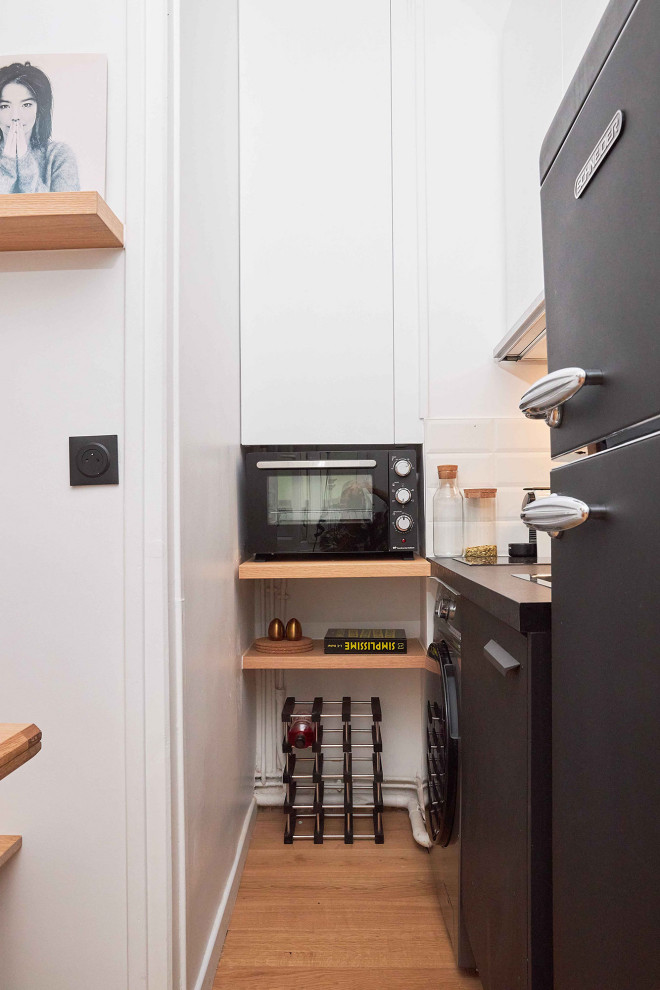 Small modern single-wall kitchen in Paris with a single-bowl sink, beaded cabinets, white cabinets, laminate countertops, white splashback, ceramic splashback, black appliances, light hardwood flooring and black worktops.