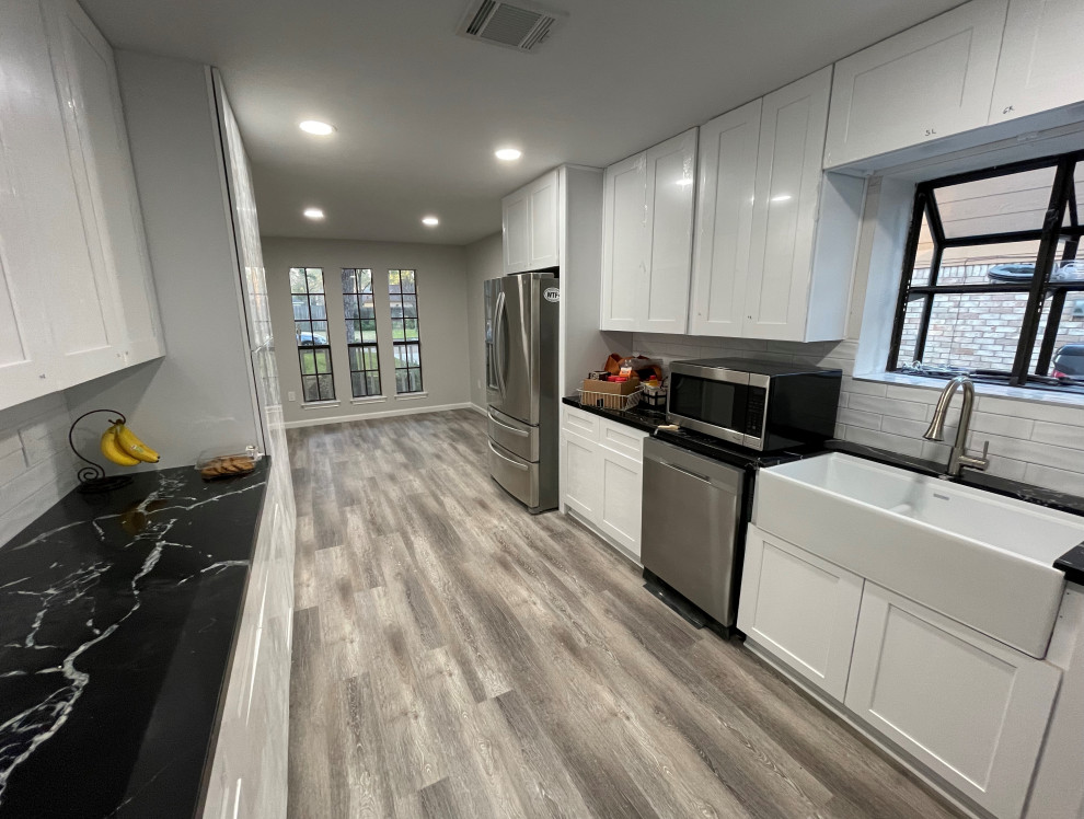 Inspiration for a large contemporary kitchen in Houston with a farmhouse sink, shaker cabinets, white cabinets, quartz benchtops, white splashback, porcelain splashback, stainless steel appliances and black benchtop.