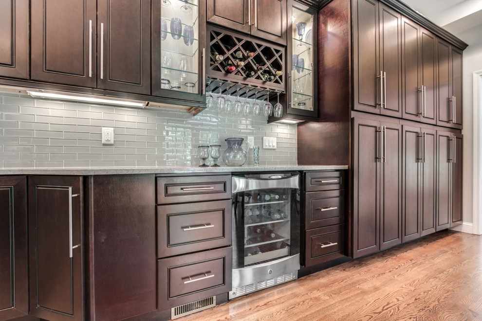 Example of a large transitional galley light wood floor and brown floor eat-in kitchen design in Raleigh with an undermount sink, raised-panel cabinets, dark wood cabinets, quartz countertops, gray backsplash, glass tile backsplash, stainless steel appliances, an island and gray countertops