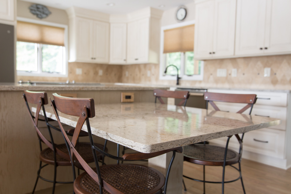Inspiration for a transitional l-shaped light wood floor eat-in kitchen remodel with an undermount sink, raised-panel cabinets, white cabinets, beige backsplash, stainless steel appliances, an island and beige countertops