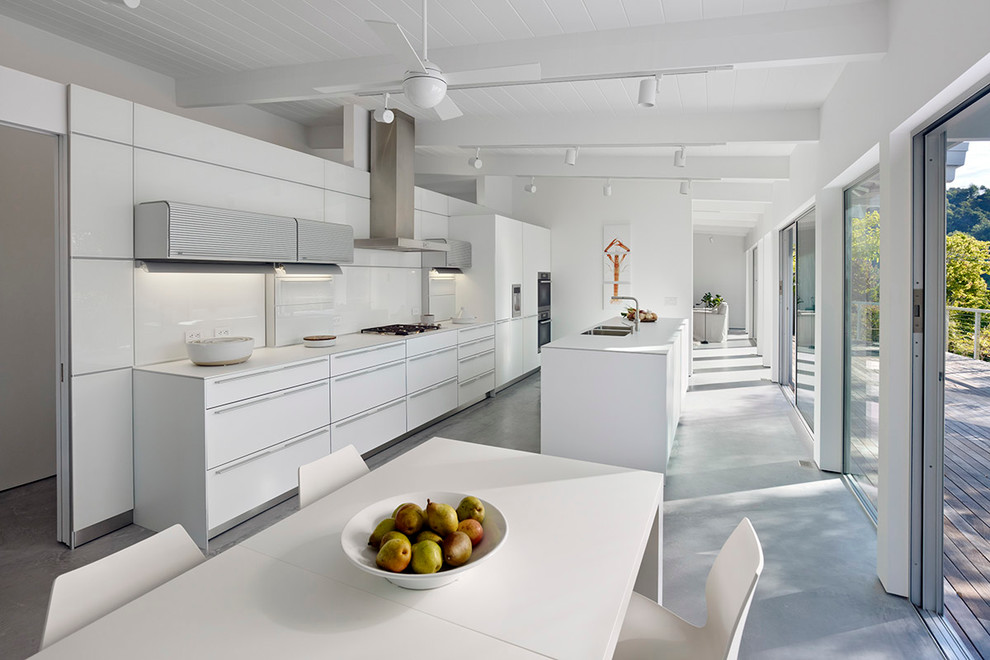 Modern galley eat-in kitchen in San Francisco with an undermount sink, flat-panel cabinets, white cabinets, laminate benchtops, white splashback, glass sheet splashback, stainless steel appliances, concrete floors and with island.