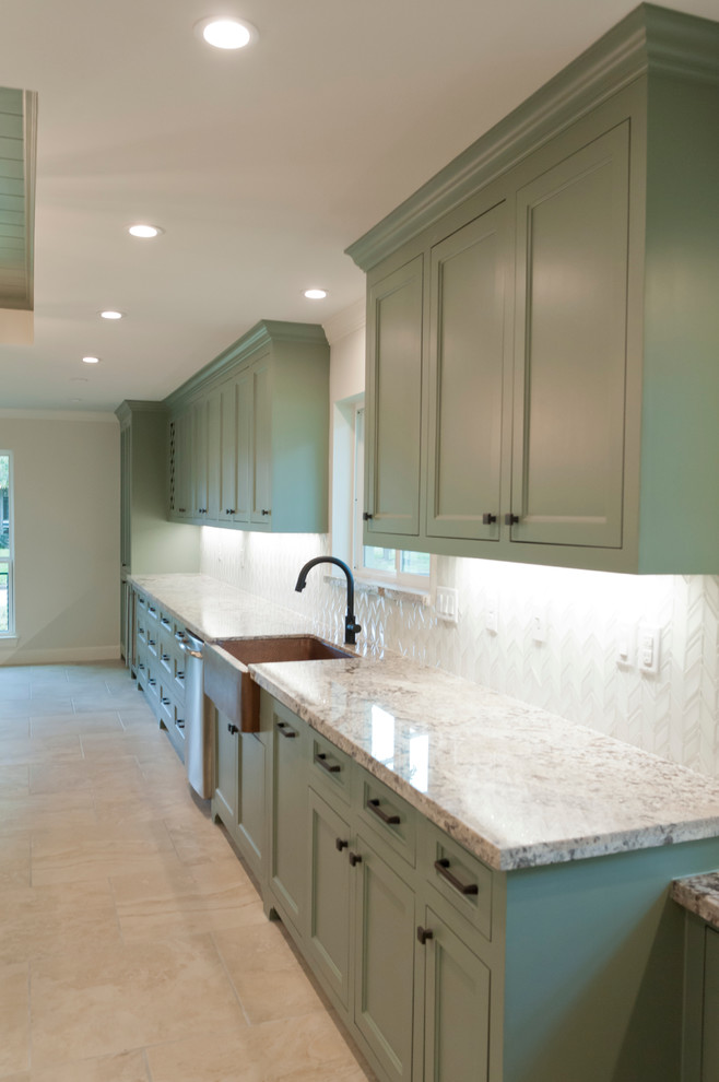 Inspiration for a large tropical galley kitchen in Houston with a farmhouse sink, recessed-panel cabinets, green cabinets, granite benchtops, white splashback, glass tile splashback, stainless steel appliances, porcelain floors and with island.