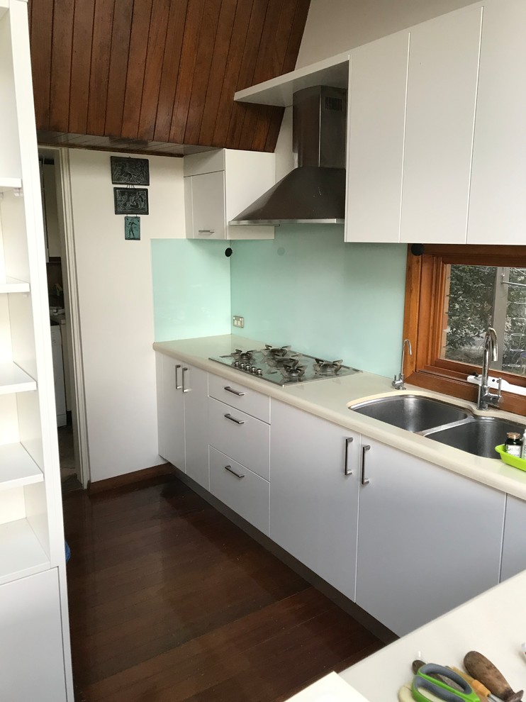 Contemporary l-shaped kitchen in Sydney with flat-panel cabinets, white cabinets, blue splashback, glass sheet splashback and stainless steel appliances.