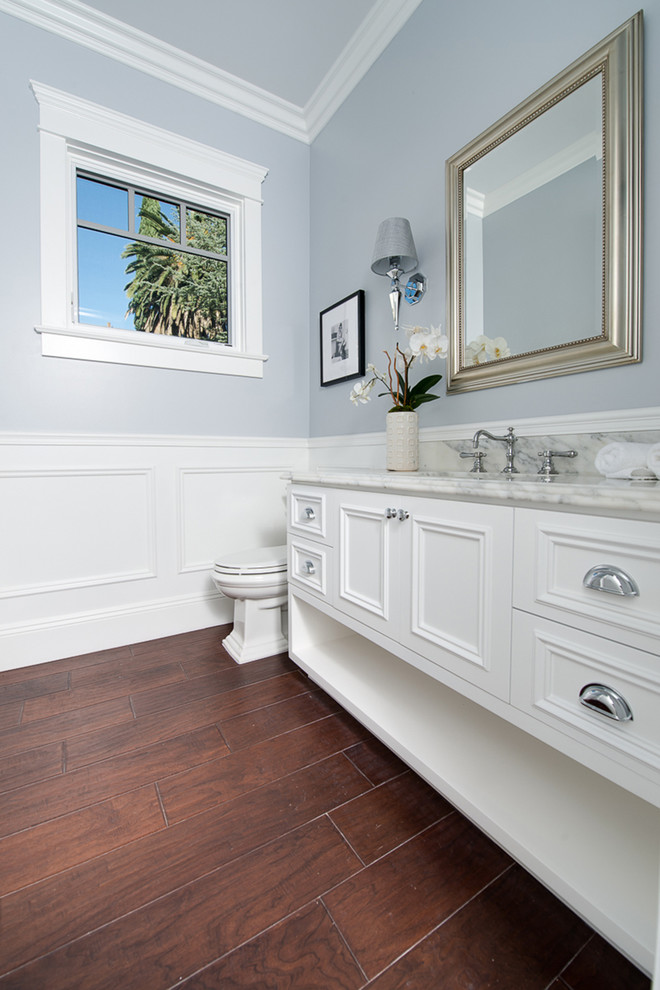 Example of a large beach style dark wood floor powder room design in Los Angeles with white cabinets, an undermount sink, marble countertops and recessed-panel cabinets