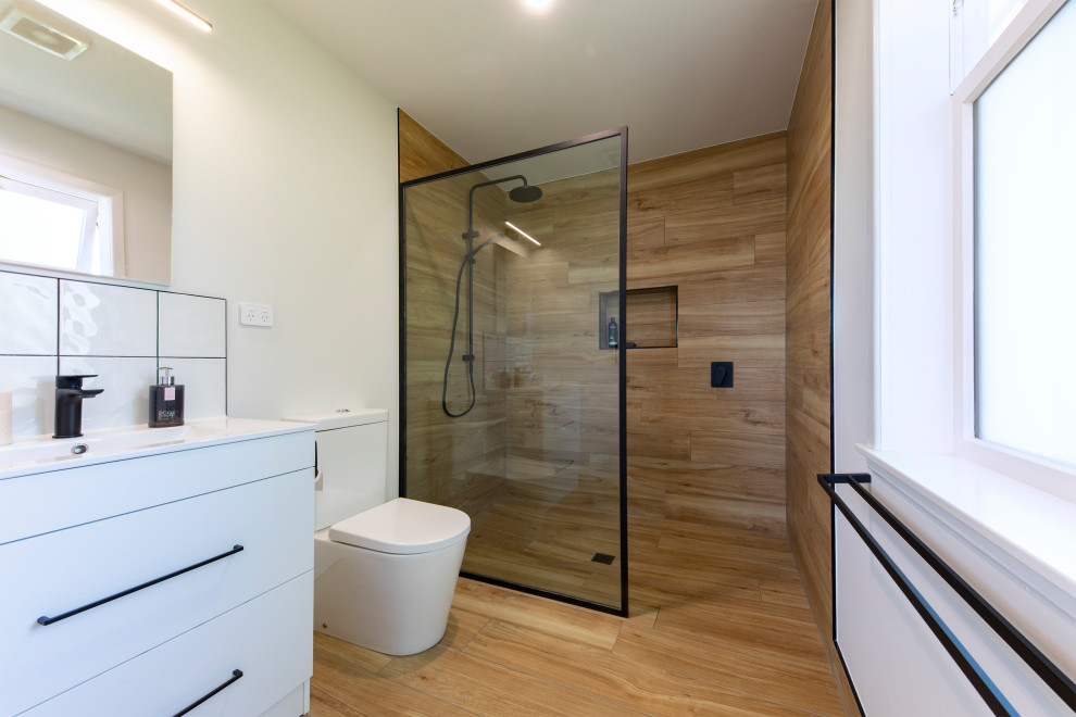 Inspiration for a large contemporary master bathroom in Auckland with flat-panel cabinets, white cabinets, an open shower, a two-piece toilet, multi-coloured tile, wood-look tile, white walls, wood-look tile, an integrated sink, engineered quartz benchtops, brown floor, an open shower, white benchtops and a built-in vanity.