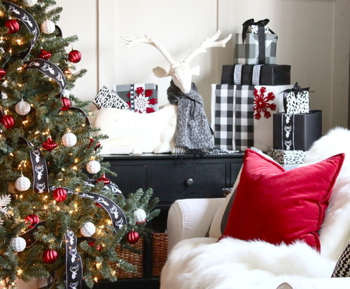 Holiday Decor Ideas for Dog Lovers - Living room with white walls, black hutch, white chair and a cristmas tree.  The hutch has presents wrapped in back and white with plaid ribbon.  The chair has a red pillow.  