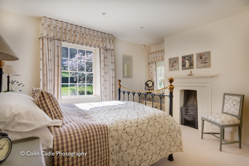 This is an example of a mid-sized country master bedroom in Devon with beige walls, carpet, a standard fireplace and a wood fireplace surround.