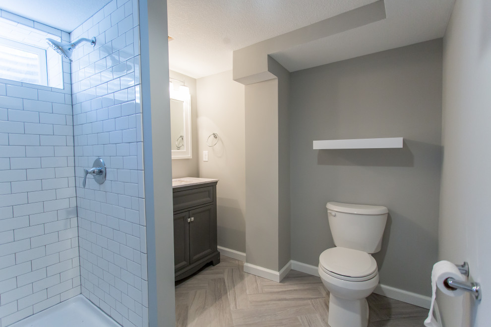 Idée de décoration pour une grande salle d'eau craftsman avec un placard à porte shaker, des portes de placard grises, un espace douche bain, WC séparés, un carrelage blanc, un carrelage métro, un mur gris, un sol en carrelage imitation parquet, un lavabo encastré, un sol gris, un plan de toilette blanc, meuble simple vasque et meuble-lavabo sur pied.