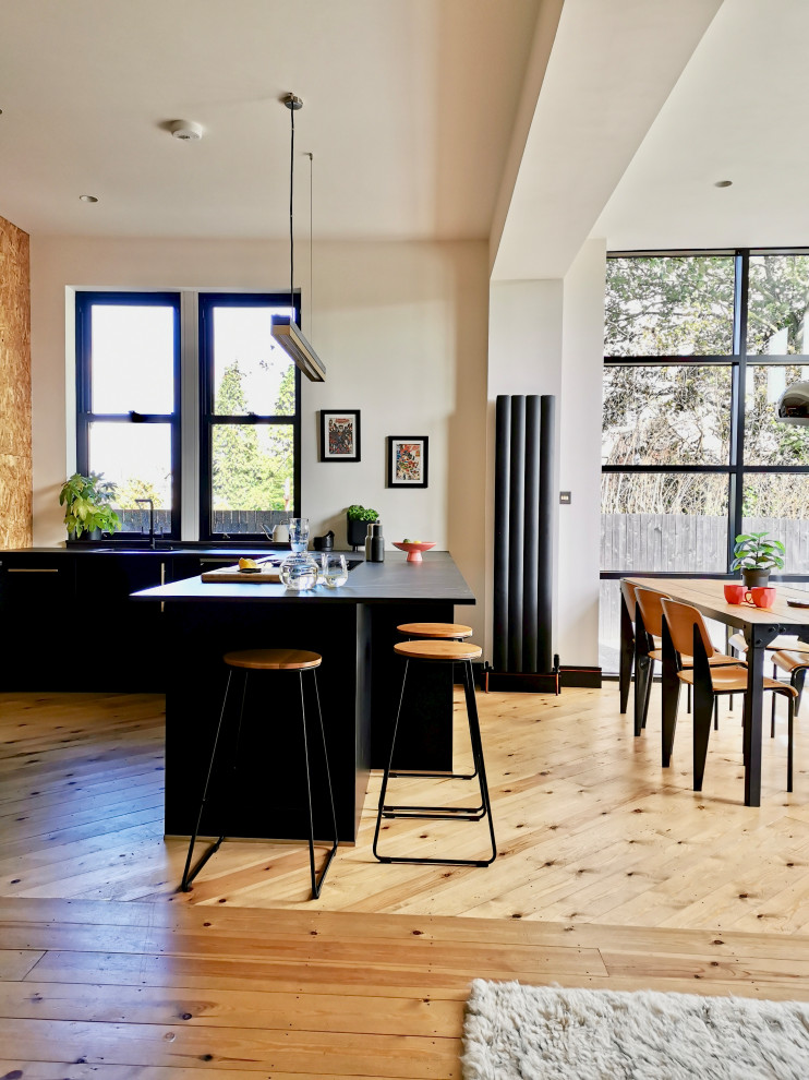 Mid-sized scandinavian u-shaped eat-in kitchen in Other with a double-bowl sink, flat-panel cabinets, black cabinets, quartzite benchtops, panelled appliances, light hardwood floors and black benchtop.