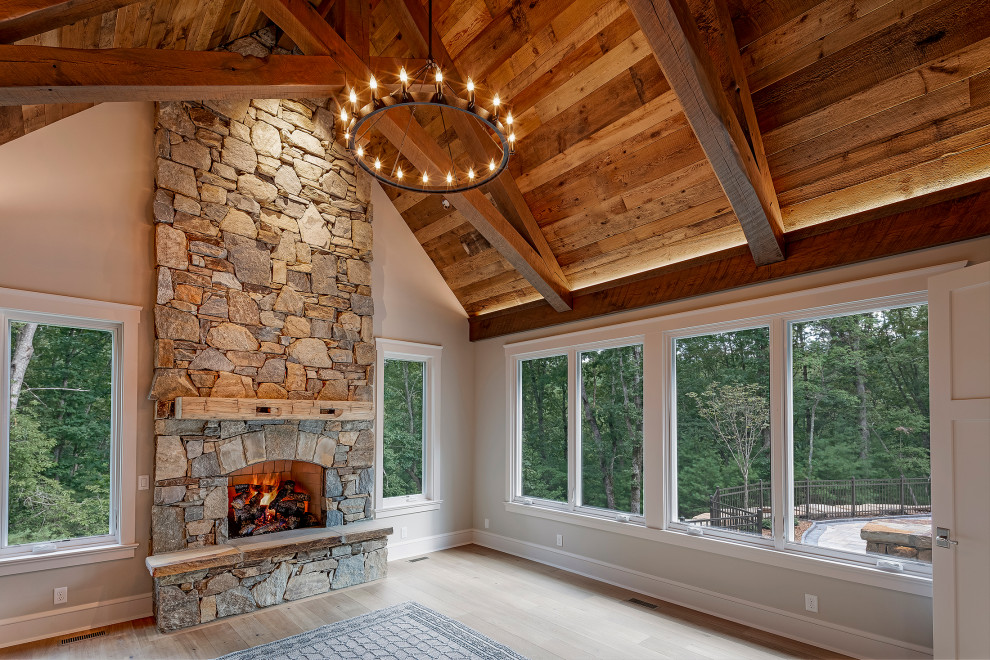 Cette image montre une grande chambre parentale chalet avec un mur gris, un sol en bois brun, une cheminée standard, un manteau de cheminée en pierre, un sol gris et un plafond en lambris de bois.