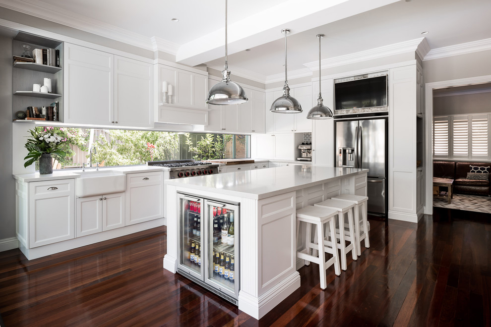 This is an example of a mid-sized transitional l-shaped eat-in kitchen in Perth with shaker cabinets, white cabinets, quartz benchtops, white splashback, window splashback, stainless steel appliances, with island, a farmhouse sink, dark hardwood floors and brown floor.