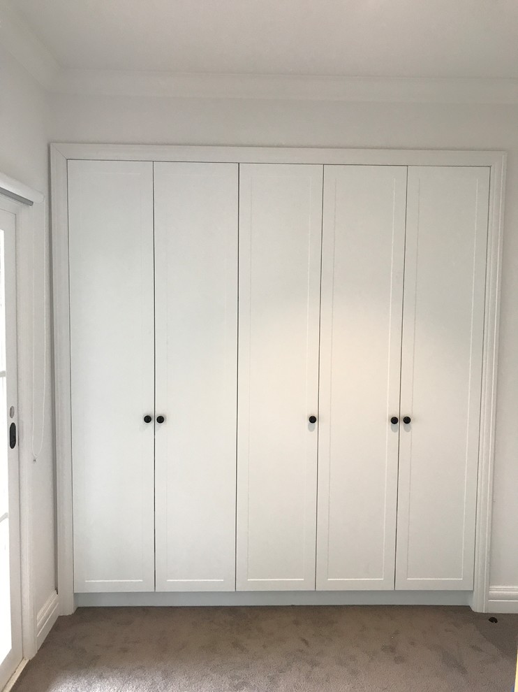 This is an example of a small traditional gender-neutral built-in wardrobe in Melbourne with recessed-panel cabinets, white cabinets, carpet and brown floor.