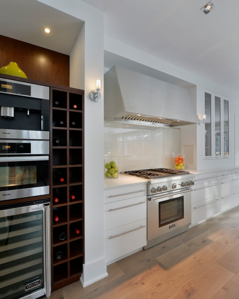 Contemporary kitchen in Ottawa with flat-panel cabinets, white cabinets, white splashback, glass sheet splashback and medium hardwood floors.