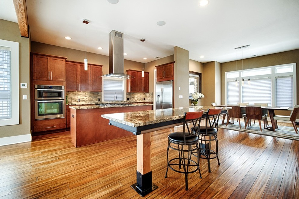 Large transitional l-shaped bamboo floor and brown floor kitchen pantry photo in Seattle with granite countertops, an undermount sink, raised-panel cabinets, medium tone wood cabinets, gray backsplash, stone tile backsplash, stainless steel appliances and two islands