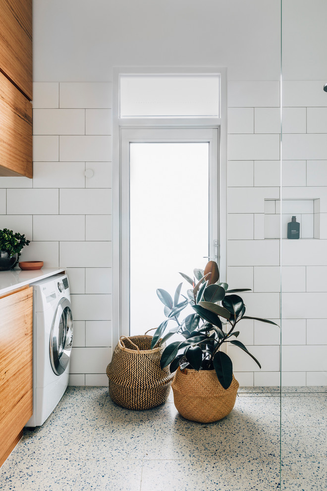 Inspiration for a contemporary single-wall laundry room in Melbourne with flat-panel cabinets, medium wood cabinets, white walls, white floor and white benchtop.