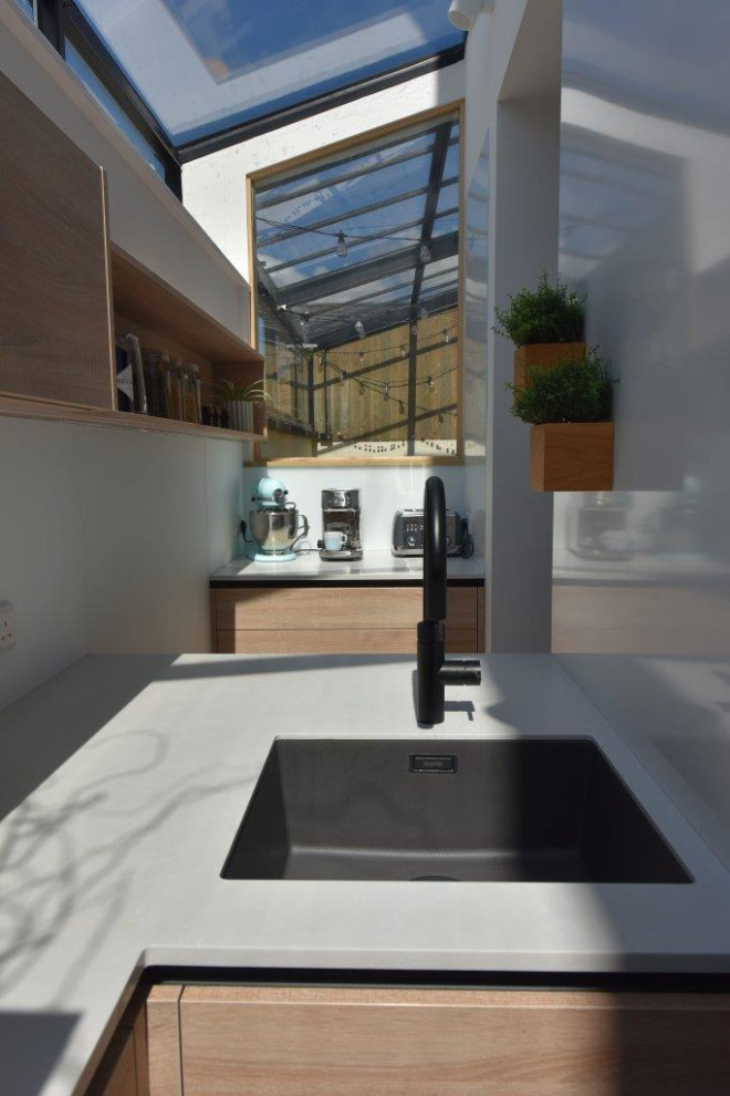 Idéer för ett mycket stort modernt vit kök, med en undermonterad diskho, skåp i ljust trä, bänkskiva i kvartsit, vitt stänkskydd, glaspanel som stänkskydd, svarta vitvaror, betonggolv, en köksö och grått golv
