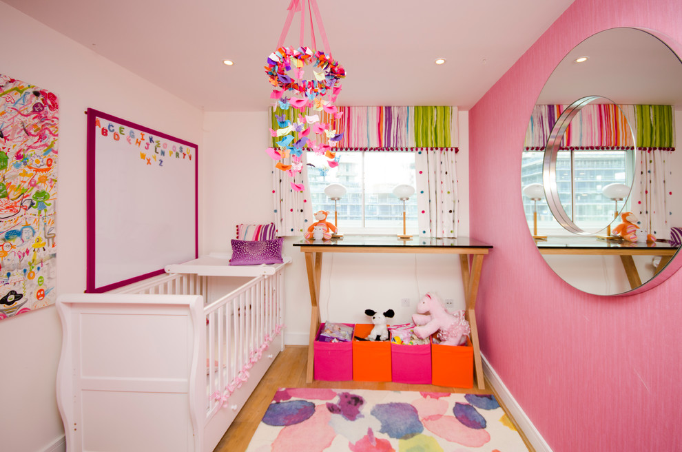 Small transitional nursery in London with pink walls and medium hardwood floors for girls.