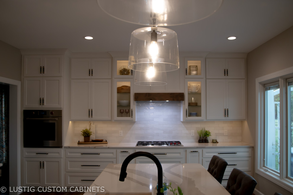 Example of a large transitional l-shaped laminate floor and brown floor open concept kitchen design with an undermount sink, flat-panel cabinets, white cabinets, quartz countertops, white backsplash, ceramic backsplash, stainless steel appliances, an island and white countertops