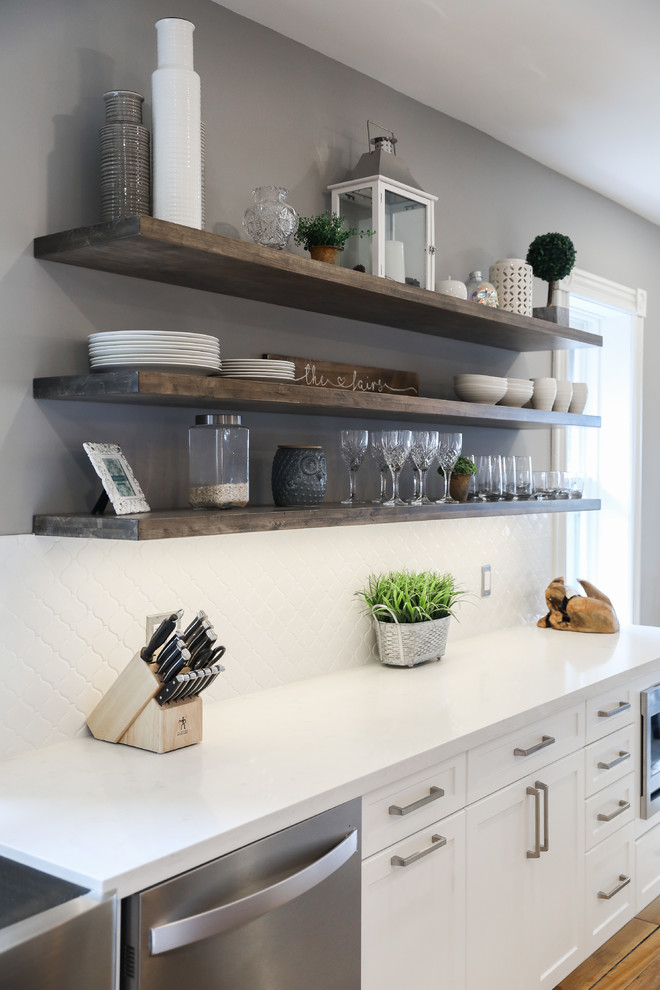 Mid-sized transitional single-wall medium tone wood floor and brown floor eat-in kitchen photo with a farmhouse sink, shaker cabinets, white cabinets, white backsplash, stainless steel appliances, an island and white countertops