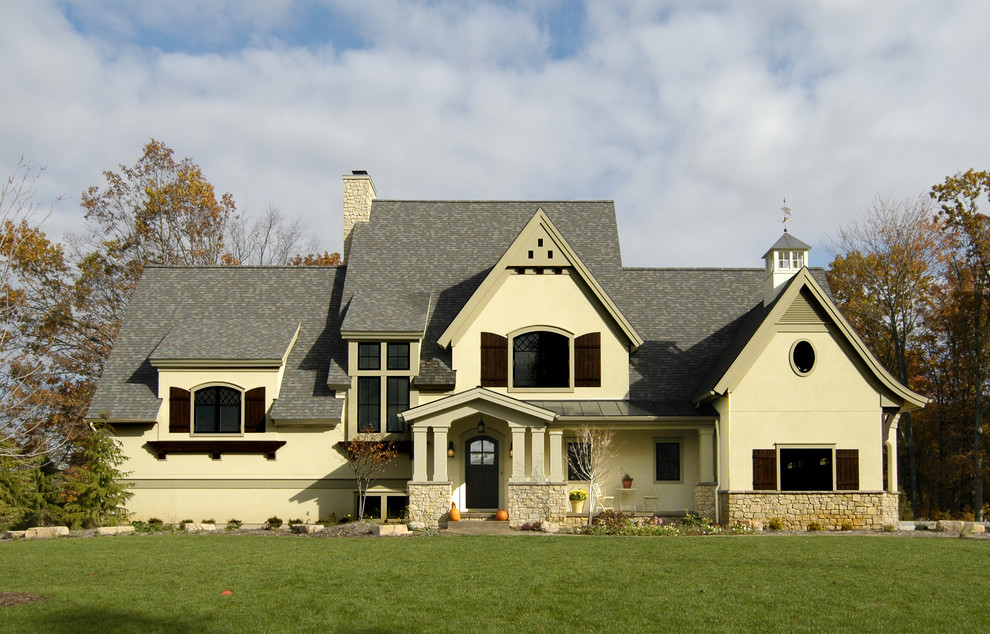This is an example of a country two-storey stucco beige house exterior in Grand Rapids with a gable roof and a shingle roof.