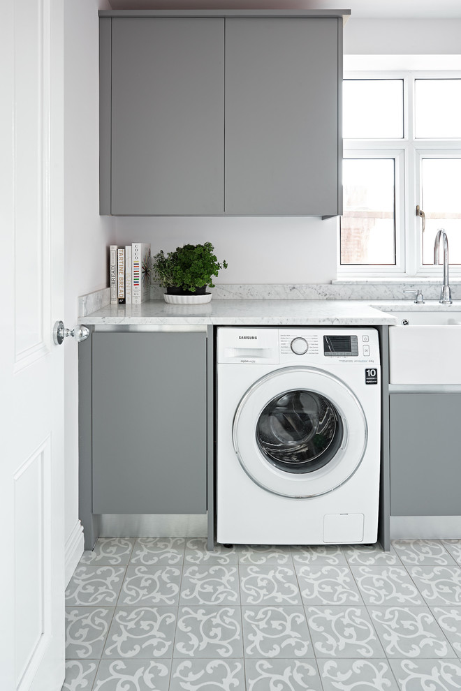 This is an example of a small transitional single-wall laundry room in Wiltshire with a farmhouse sink, flat-panel cabinets, grey cabinets, marble benchtops, ceramic floors and grey floor.