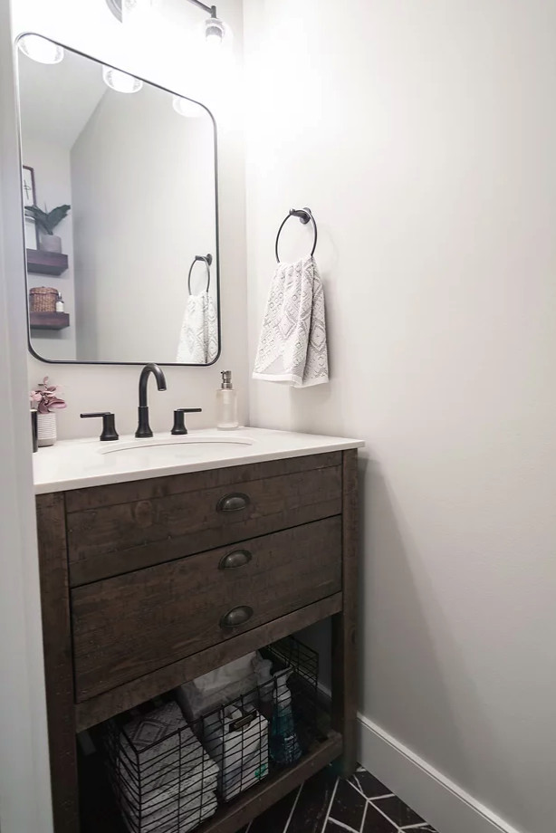 Small transitional ceramic tile and black floor powder room photo in Minneapolis with shaker cabinets, brown cabinets, a wall-mount toilet, gray walls, an integrated sink, quartz countertops, white countertops and a freestanding vanity