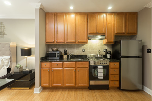 Studio kitchenette with warm wood shaker kitchen cabinet uppers extended to the ceiling (≈42"), maximizing vertical storage above a compact range and fridge
