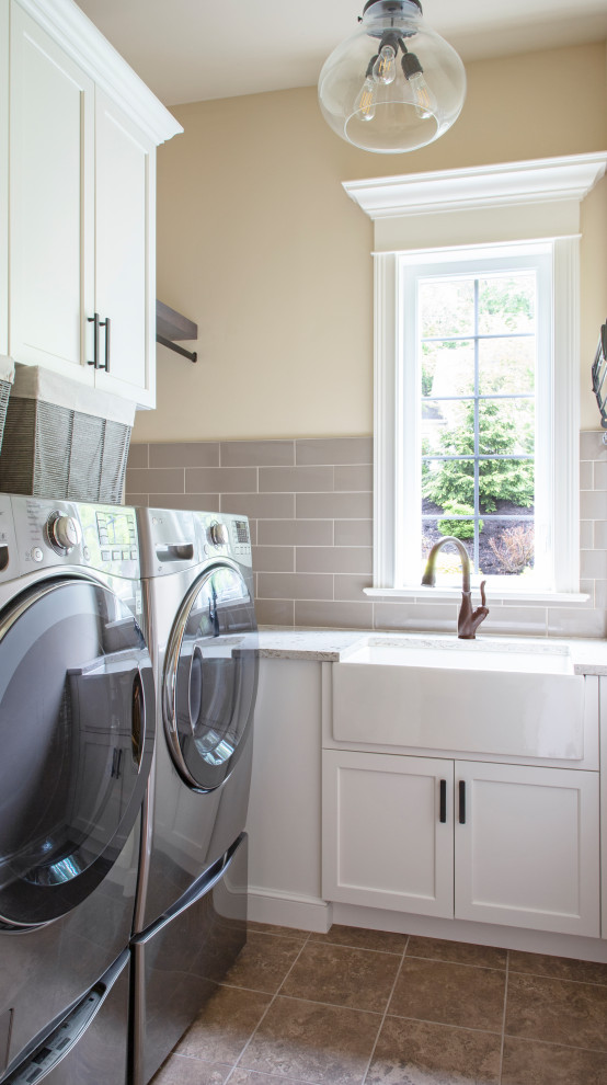Example of a transitional ceramic tile and beige floor laundry room design with a farmhouse sink, shaker cabinets, white cabinets, quartz countertops, beige walls and a side-by-side washer/dryer