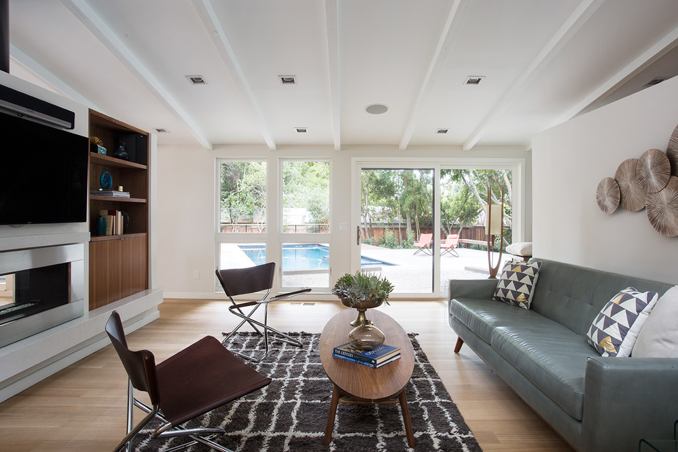 This is an example of a midcentury family room in San Francisco with white walls, medium hardwood floors, a two-sided fireplace and a wall-mounted tv.