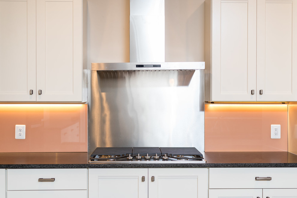 Example of a transitional u-shaped eat-in kitchen design in DC Metro with a double-bowl sink, shaker cabinets, white cabinets, granite countertops, brown backsplash, glass sheet backsplash, stainless steel appliances, an island and black countertops