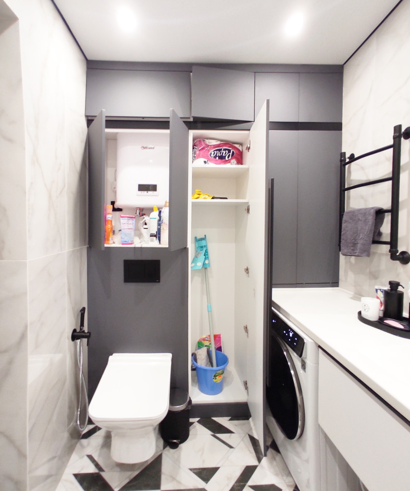 Small contemporary master bathroom in Other with flat-panel cabinets, grey cabinets, an undermount tub, a wall-mount toilet, white tile, marble, white walls, porcelain floors, an integrated sink, solid surface benchtops, black floor, white benchtops, a laundry, a single vanity and a floating vanity.