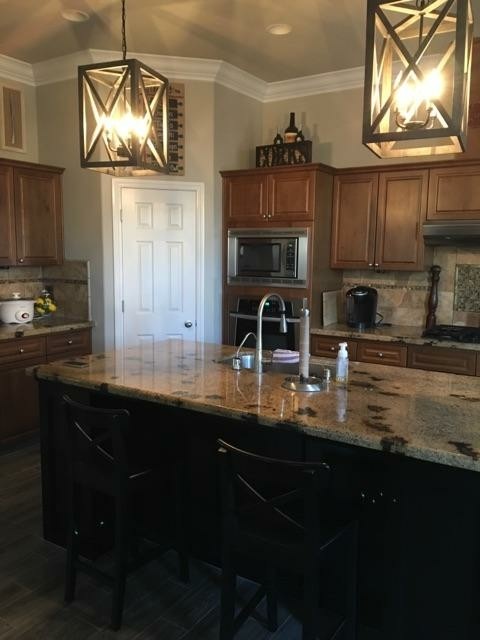 Open concept kitchen - small transitional galley laminate floor and brown floor open concept kitchen idea with an undermount sink, raised-panel cabinets, medium tone wood cabinets, granite countertops, beige backsplash, stone tile backsplash, stainless steel appliances and an island